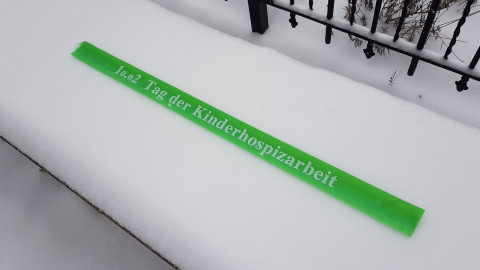 Grünes Band im Schnee mit der Aufschrift "10.02. Tag der Kinderhospizarbeit"