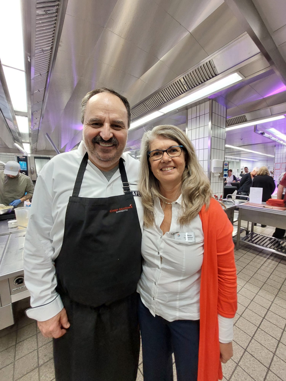 Sternekoch Johann Lafer und unsere Hauptamtliche Stefanie Schweitzer stehen Arm in Arm in der Großküche des Vinzentius Krankhauses